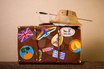 Old battered suitcase seasoned traveler with stickers from various countries he visited tropical helmet and broken through arrow.