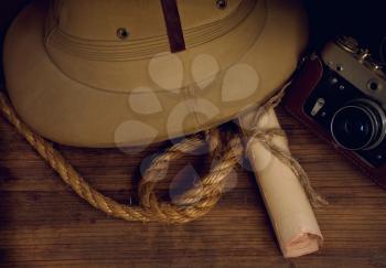 a still life with an old shabby colonial cork helmet with a folded map and a camera on a wooden background