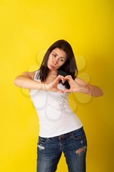 Pretty girl with dark hair in casual clothes folded her symphol of the heart from her fingers, but not very happy judging by the grimace