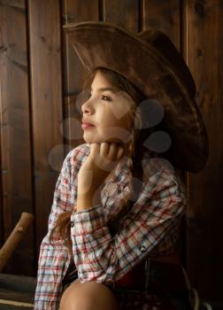 Little girl in a wide-brimmed cowboy hat and traditional dress posing on a dark wooden background