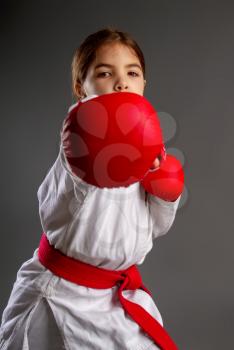Little girl in red sport gloves in red belt and white kimono strikes with her right hand