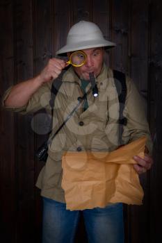 a traveler in a cork helmet and khaki clothes looking at an old map highlighting a flashlight