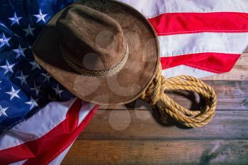 brown classic cowboy hat, coarse rope and big american flag lying on dark boards
