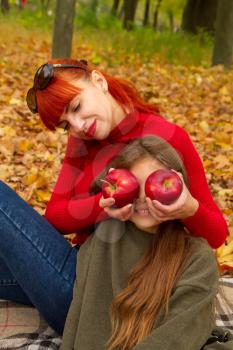 young mother and little daughters in bright sweaters on a picnic in nature indulge in apples