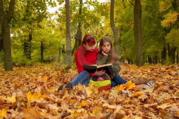 young mother and little daughters in bright sweaters on a picnic in nature read a book together