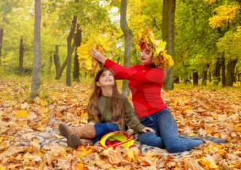 mom and daughter on a picnic in autumn park on the background of fallen yellow leaves in wreaths of maple