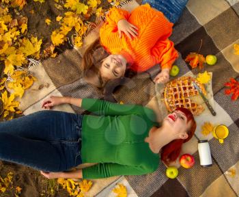 young mother and little daughters in bright sweaters on a picnic in nature relax