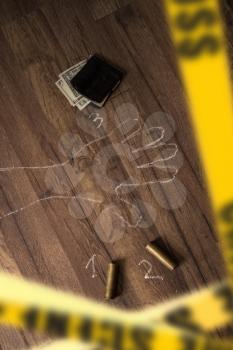 Crime scene fenced with yellow police tapes with a silhouette of the victim painted on the floor with chalk and brass sleeves from a hunting rifle.