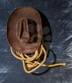 classic brown wide-brimmed cowboy hat and rough lasso rope hang on a dark wooden wall