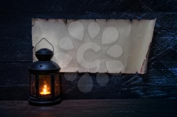vintage horizontal parchment on a dark wooden wall with place for your text and a lantern with a candle nearby