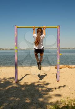 Little girl goes in for sports outdoors pulls herself up on horizontal bars