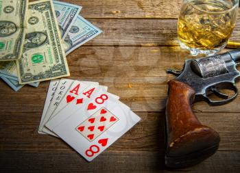 playing cards laid out on an old wooden table in the saloon money, whiskey and a revolver for self-defense