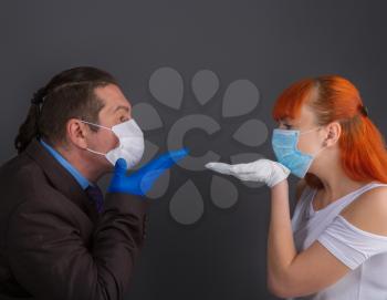 A man in a suit and a girl make an air kiss on a dark background through protective medical masks and gloves.