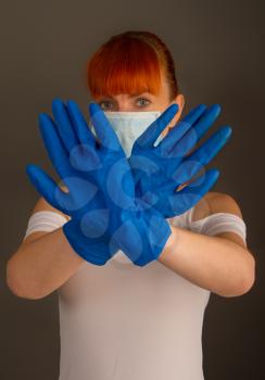 Young girl in medical mask and rubber protective gloves shows a prohibition sign with her hands.