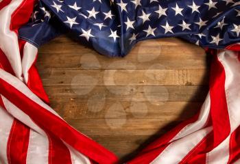 Star-striped flag of the United States of America stacked in the form of a heart on an old wooden background