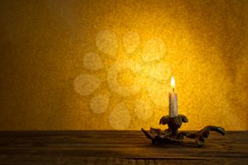 Lonely burning candle in a candlestick on a dark brown background