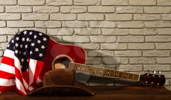 the traditional wide-brimmed cowboy hat, and the stars-striped US flag lie next to a classic acoustic guitar