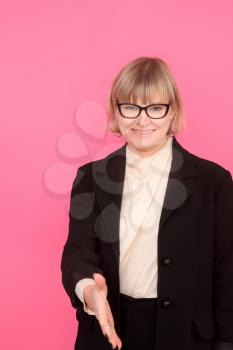 business woman in a formal suit and glasses affably extends her hand to her interlocutor on a pink background