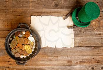 blank sheet of yellowed old papyrus Leprechaun hat, horseshoe and pot of coins. On a rough wooden background
