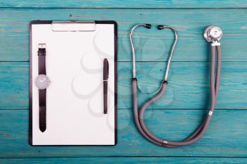 Workplace of doctor - stethoscope, medicine clipboard, pen and watches on wooden desk