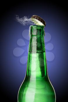 Cold wet open beer bottle with smoke on blue background