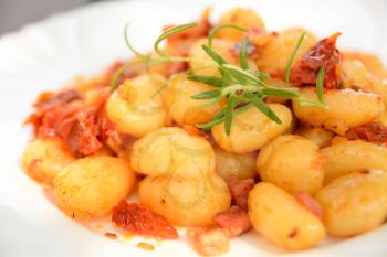 Gnocchi with tomatoes, bacon and onion on the white plate.
