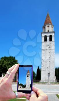 View over the mobile phone display during taking a picture of Basilica of Aquileia in Italy. Holding the mobile phone in hands and taking a photo of Basilica of Aquileia. Focused on mobile phone scree
