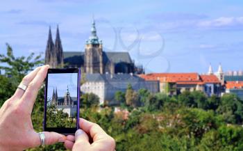 View over the mobile phone display during taking a picture of Prague Castle in Prague. Holding the mobile phone in hands and taking a photo. Focused on mobile phones screen. 