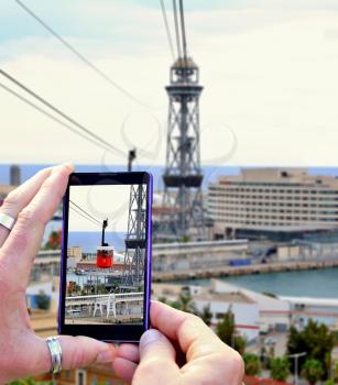 View over the mobile phone display during shooting cable car in Barcelona. Holding the mobile phone in hands and taking a photo, focused on mobile phone screen.