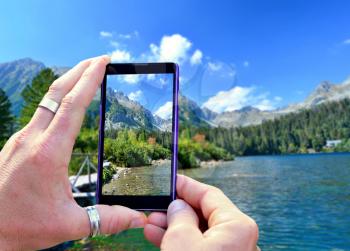 View over the mobile phone display during shooting nature of High Tatras. Holding the mobile phone in hands and taking a photo, focused on mobile phone screen.