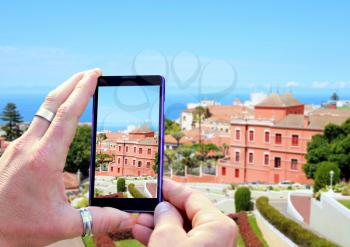 View over the mobile phone display during taking a picture of castle and garden Victoria in La Orotava, Tenerife. Holding the mobile phone in hands and taking a photo. Focused on mobile phone screen. 