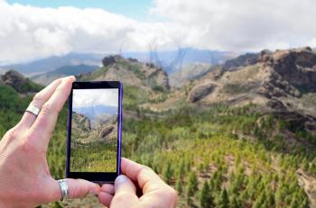 View over the mobile phone display during taking a picture of mountains in Gran Canaria. Holding the mobile phone in hands and taking a photo. Focused on mobile phone screen. 