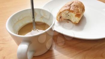 Breakfast with coffee and fresh croissant on a white plate.
