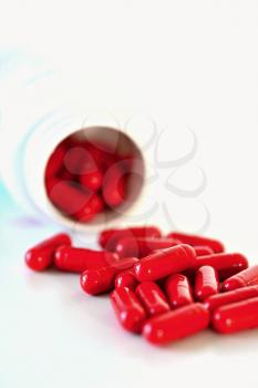Red capsules spilled out of a container on white background.