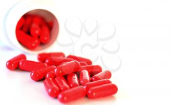 Red capsules spilled out of a container on white background.