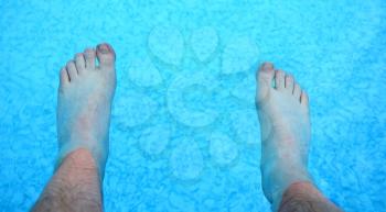 Top view on the feet refreshing in a clear water in the swimming pool.