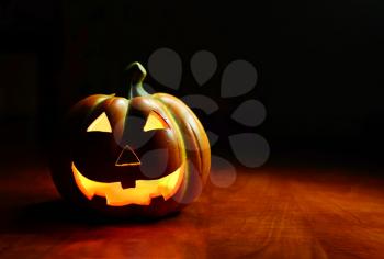 Illuminated Halloween smiling spooky pumpkin on a dark background.