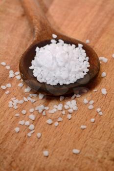 White clear salt crystals on a wooden spoon.
