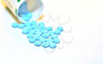 Closeup of a Blue Drug Pills Spilling Out of a Bottle on the White Background.