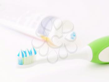 Toothbrush head with toothpaste and toothpaste tube on white background. Focused on foreground. Shallow depth of field