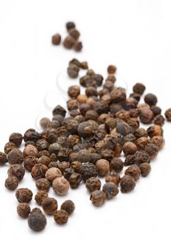 Closeup of whole black peppercorns on white background.