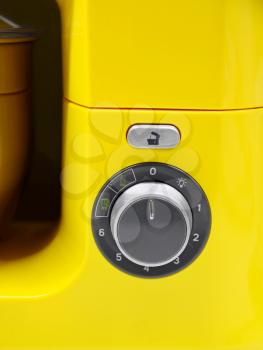 Part of yellow kitchen cooking machine, closeup of manual control and button.