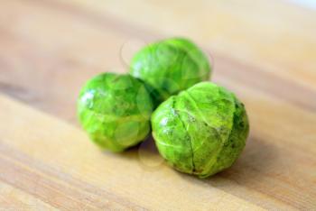 Group of three whole fresh brussels sprouts on wooden plate.