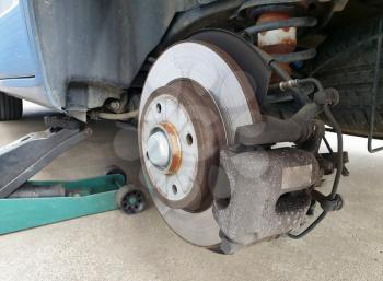 Close up of a car disc brake and a jack during car maintenance. Close up of disc brake without the wheel, car lifted on a jack.