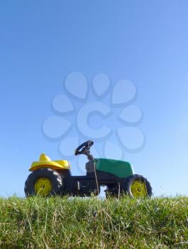 Childhood toy pedal tractor car standing on green grass with blue sky background.