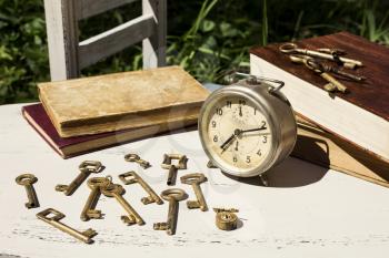 Vintage still life with old alarm clock, keys and books on a white wooden table 