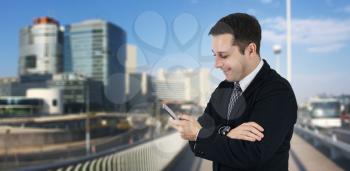 Businessman Holding Phone While Smiling and Feeling Happy With Business City and Corporate Buildings In Background