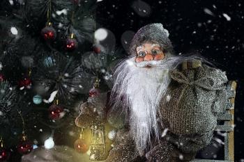 Santa Claus Outdoors Beside Christmas Tree in Snowfall Carrying Gifts to Children. Merry Christmas & New Year's Eve concept