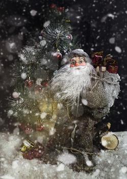 Santa Claus Outdoors Beside Christmas Tree in Snowfall Carrying Gifts to Children. Merry Christmas & New Year's Eve concept