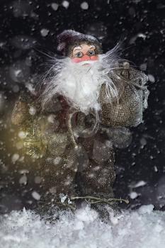 Santa Claus Outdoors Beside Christmas Tree in Snowfall Carrying Gifts to Children. Merry Christmas & New Year's Eve concept